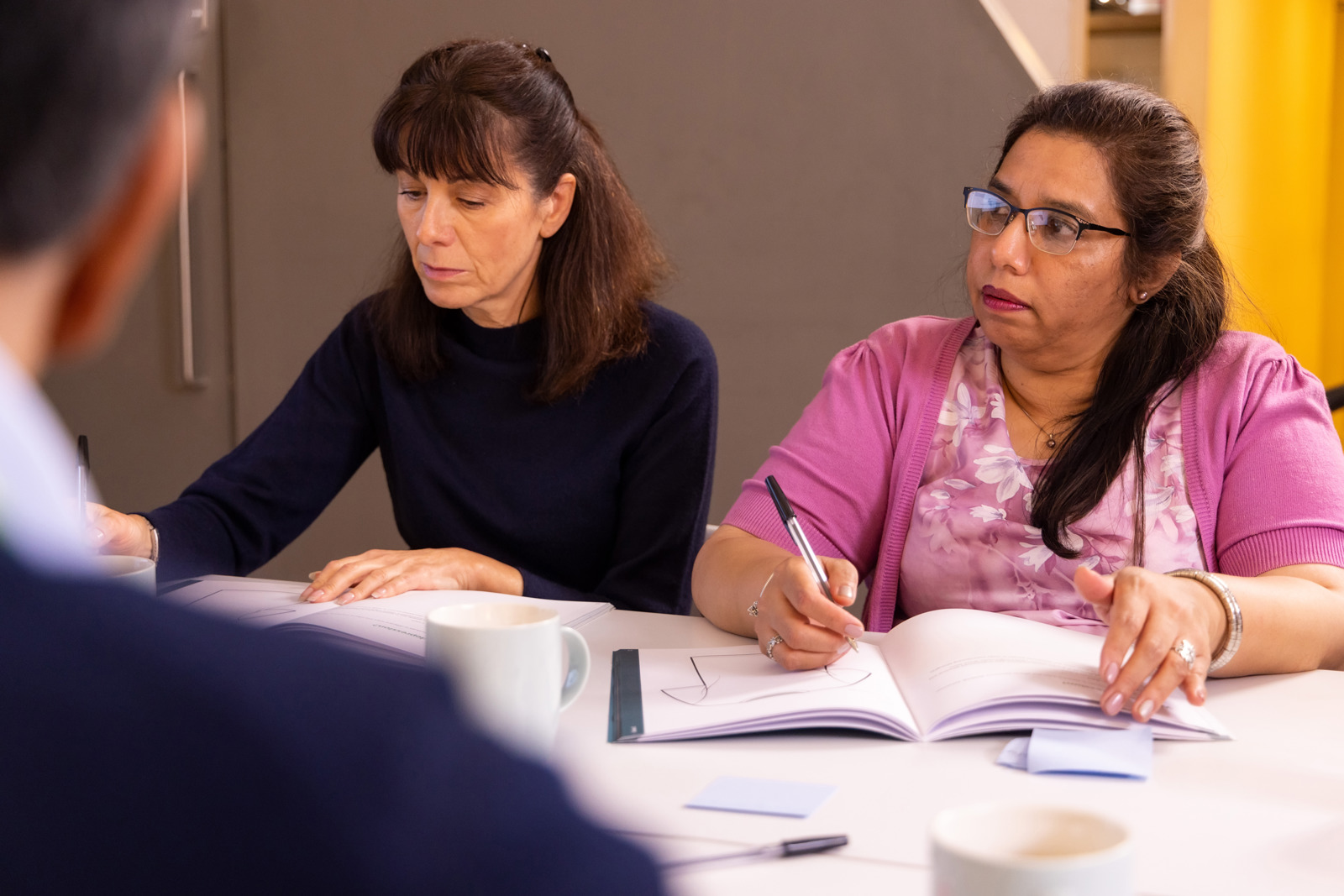 Two women sitting at a table writing 