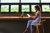 A Woman Sits At A Bar Table Next To A Window Reading A Book