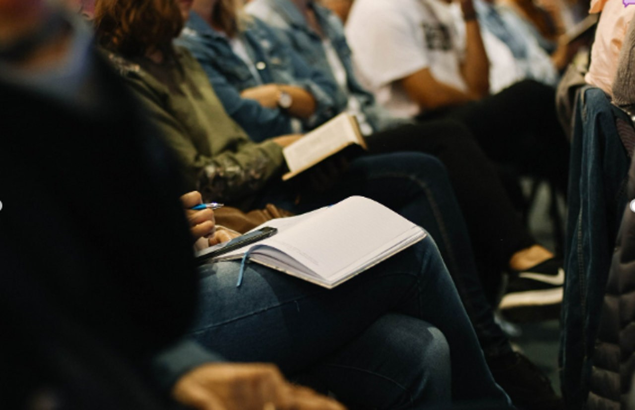 People Sat In A Line With Notebooks In Their Laps